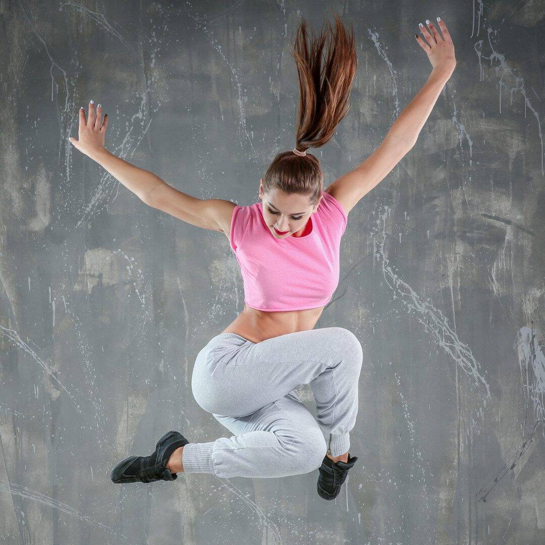 Tänzerin springt vor grauem Hintergrund.