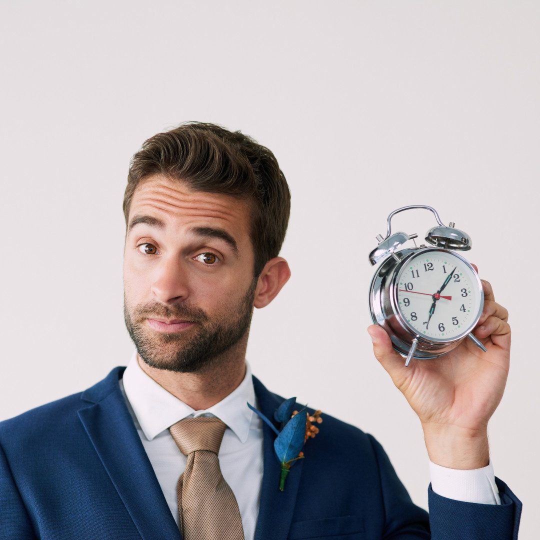 Mann im Anzug hält Wecker hoch.