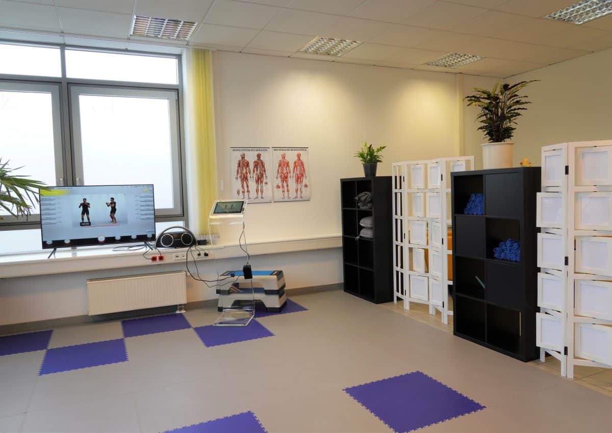 Physiotherapieraum mit Fitnessausrüstung und anatomischen Postern.