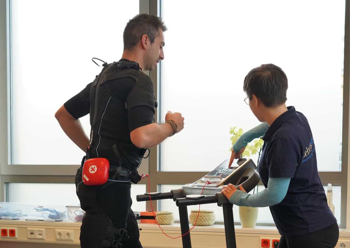 Person trainiert auf Laufband mit Physiotherapeutin.