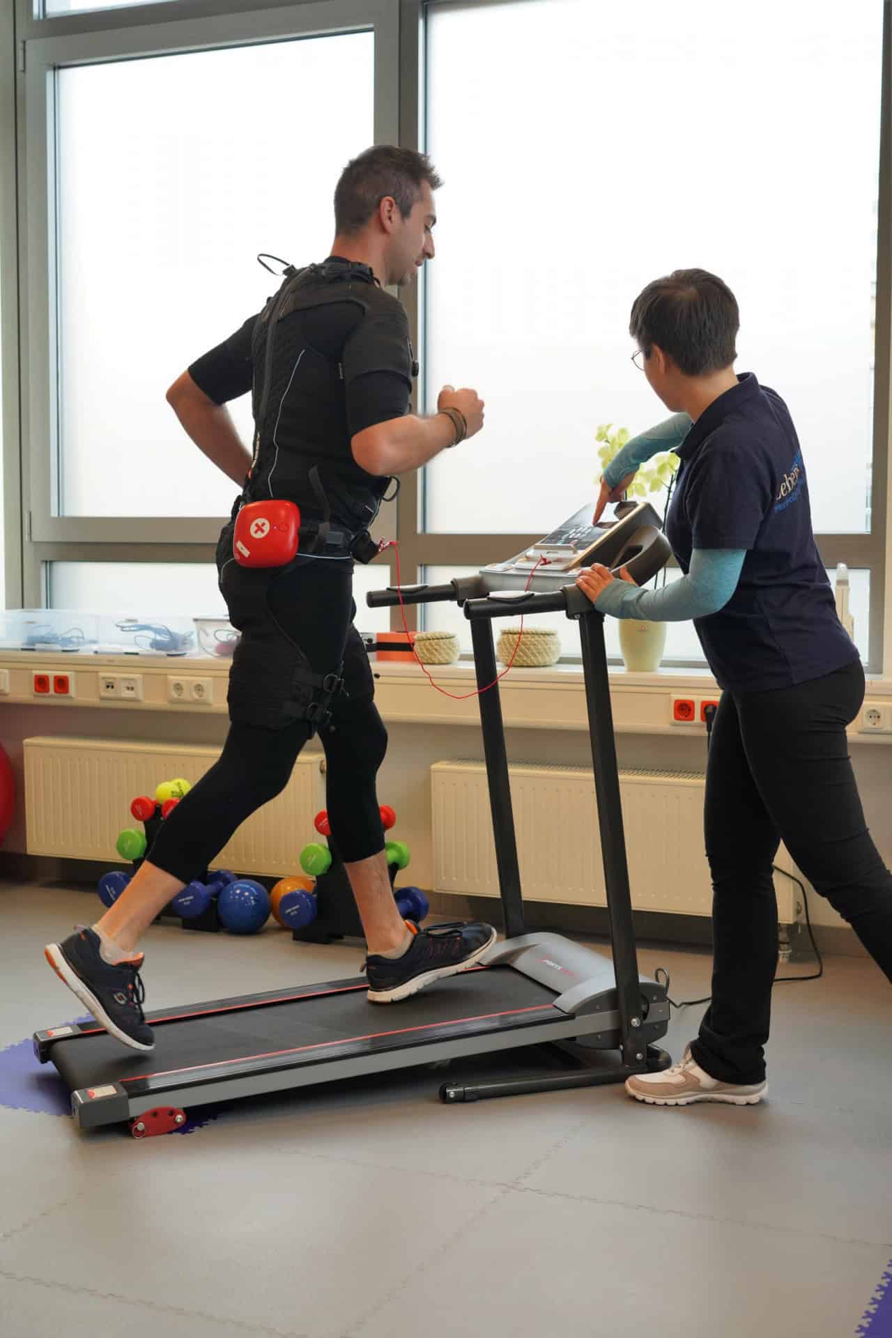 Mann läuft auf Laufband mit physiotherapeutischer Unterstützung.